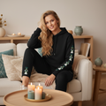Black athleisure set with teal triangle details at ankles and sleeves in cozy Scandinavian living room with fur throws and candles