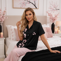 Blonde woman in black cherry blossom pajama top in cozy pink and black bedroom with candles