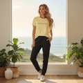 Confident woman wearing yellow t-shirt and black track pants by window in coastal home