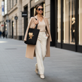 Elegant woman carrying black eagle cityscape tote bag in luxury camel coat on upscale city street - premium urban lifestyle
